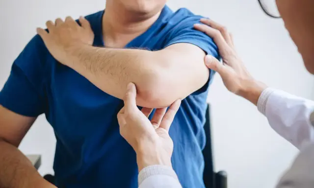 Fizjoterapeuta bada łokieć pacjenta. Dłonie specjalisty delikatnie dotykają bolącego miejsca, oceniając zakres ruchu i ból.