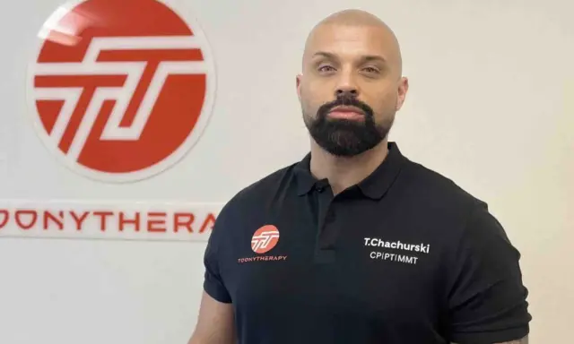 Tomasz Chachurski w czarnej koszulce z logo Toonytherapy, na tle białej ściany z logo.