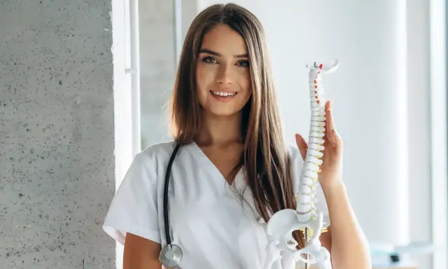 Uśmiechnięta fizjoterapeutka z modelem kręgosłupa. Zastanawia się, do kiedy studia magisterskie fizjoterapia.