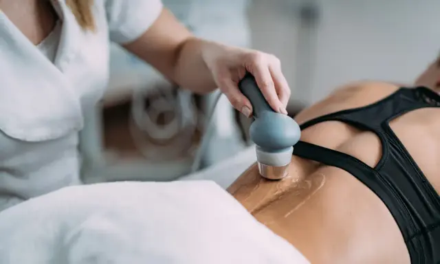 Rehabilitacja ultradźwięki na czym polega? Fizjoterapeuta wykonuje zabieg ultradźwiękami na plecach pacjentki, co pomaga w leczeniu bólu i regeneracji tkanek.