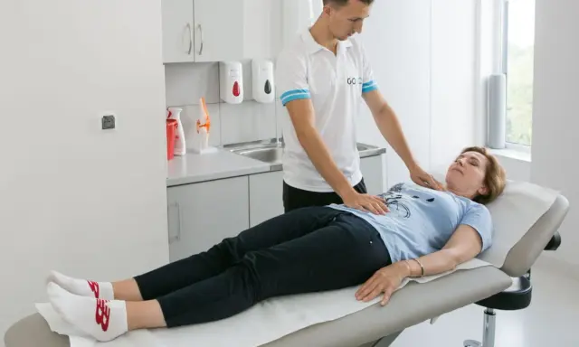 Fizjoterapeuta pomaga pacjentce w ćwiczeniach oddechowych, kładąc dłonie na jej klatce piersiowej i brzuchu.