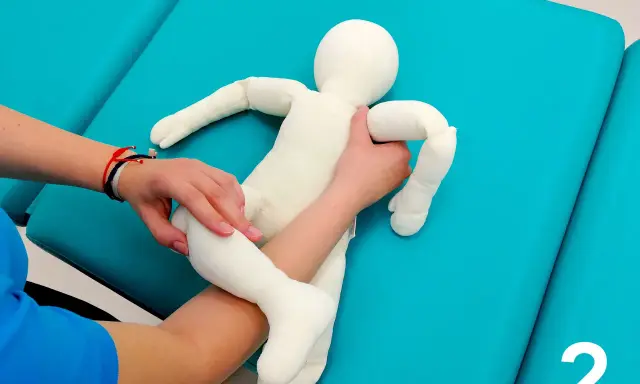 Fizjoterapeuta pokazuje mamie, jak podnosić niemowlę, trzymając pluszową lalkę.