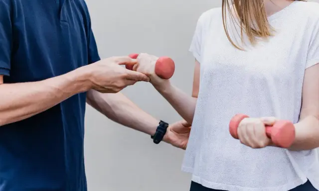 Fizjoterapeuta pomaga pacjentce ćwiczyć z hantlami. To przykład rehabilitacji, która przywraca sprawność.