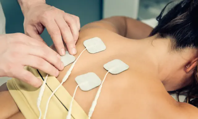 Rehabilitacja TENS: na czym polega? Fizjoterapeuta umieszcza elektrody na plecach pacjentki, co jest częścią terapii prądami TENS.