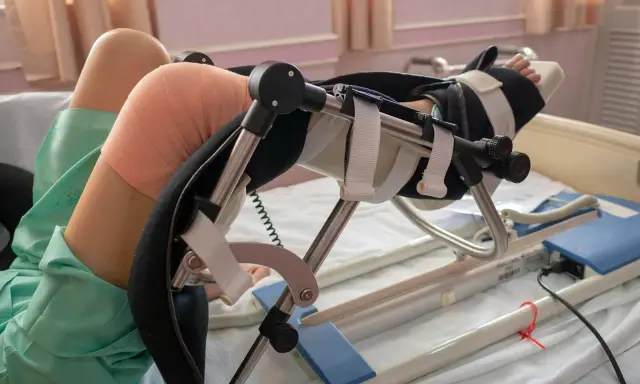 Pacjent po zabiegu z endoprotezą kolana w specjalistycznym urządzeniu rehabilitacyjnym, z bandażem na kolanie.