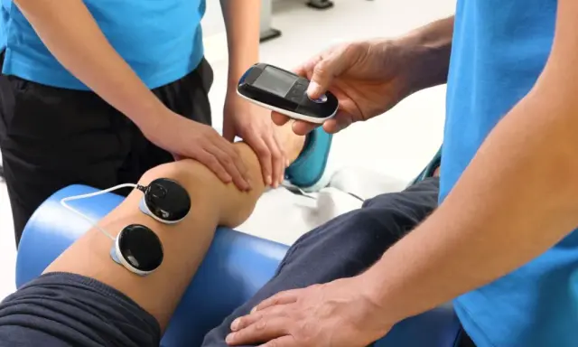 Fizjoterapeuta z urządzeniem do elektroterapii przy nodze pacjenta. Ile razy w roku można korzystać z rehabilitacji szpitalnej?