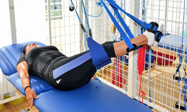 Kobieta na łóżku rehabilitacyjnym ćwiczy nogi w systemie podwieszeń. To przykład, jak wygląda rehabilitacja dzienna co to jest.