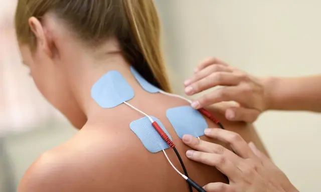 Elektrody na plecach kobiety, podłączone do urządzenia. To przykład, co to jest fizjoterapia – rehabilitacja i leczenie bólu.