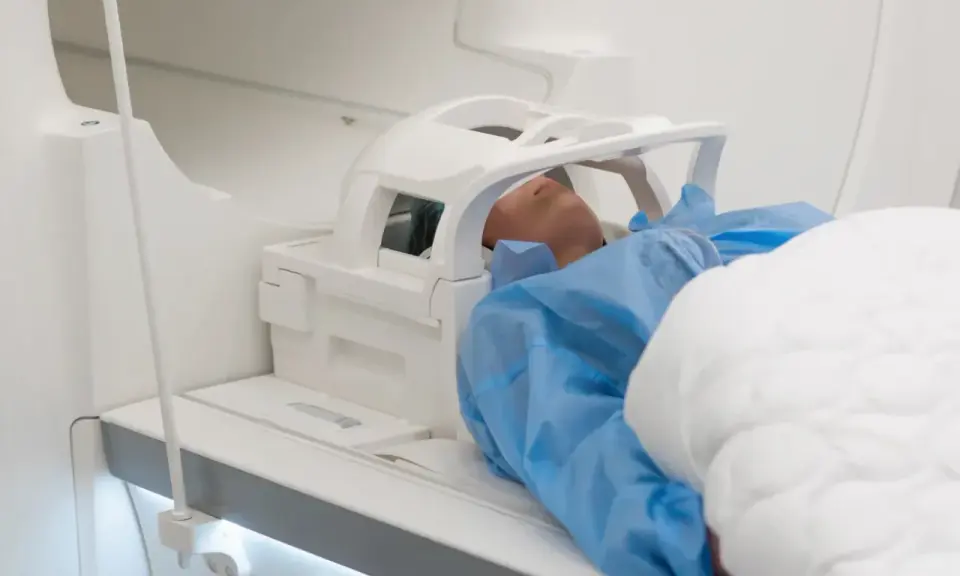 Pacjent w niebieskim fartuchu leży w aparacie MRI. Czas badania, czyli ile trwa rezonans głowy, zależy od wielu czynników.