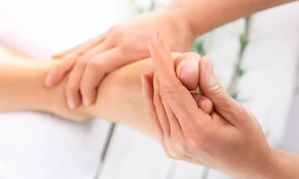 Dłoń terapeuty masuje stopę pacjenta, skupiając się na palcach.