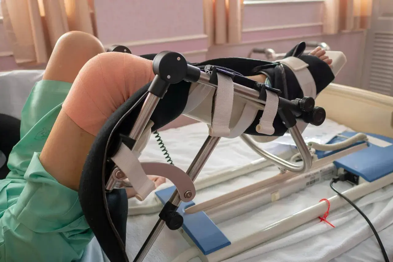 Pacjent po zabiegu z endoprotezą kolana w specjalistycznym urządzeniu rehabilitacyjnym, z bandażem na kolanie.