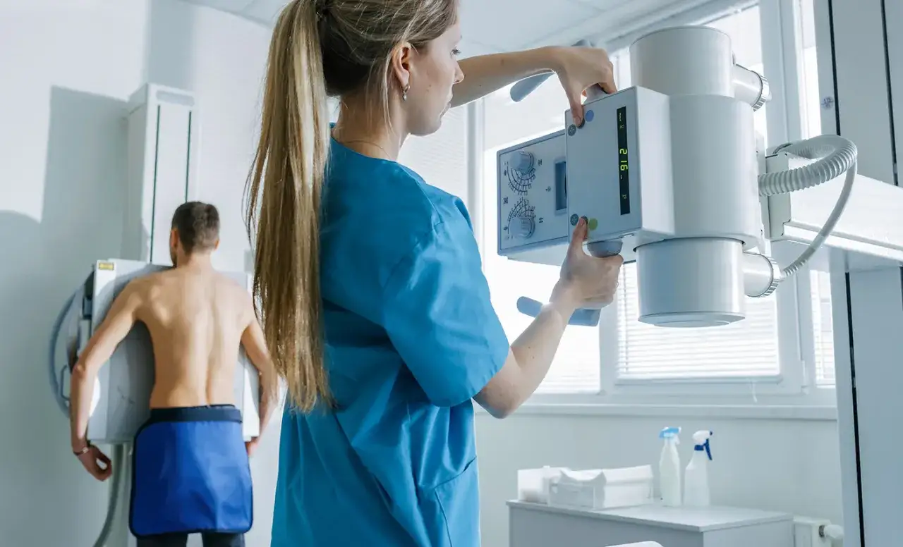 Technik przygotowuje pacjenta do wykonania rtg klatki piersiowej, ustawiając aparat rentgenowski.