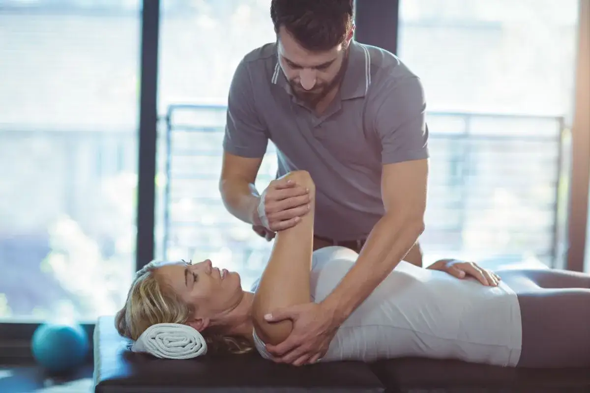 Fizjoterapeuta wykonuje ćwiczenia z pacjentką. Czy fizjoterapeuta a rehabilitant to to samo? Tak, to te same specjalizacje.