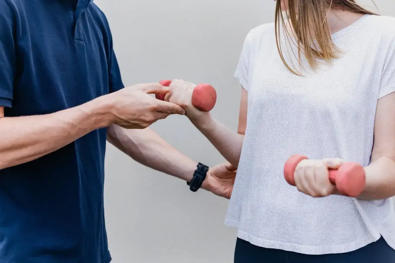 Fizjoterapeuta pomaga kobiecie ćwiczyć z hantlami. Czy fizjoterapeuta to lekarz? To specjalista od rehabilitacji, nie lekarz.