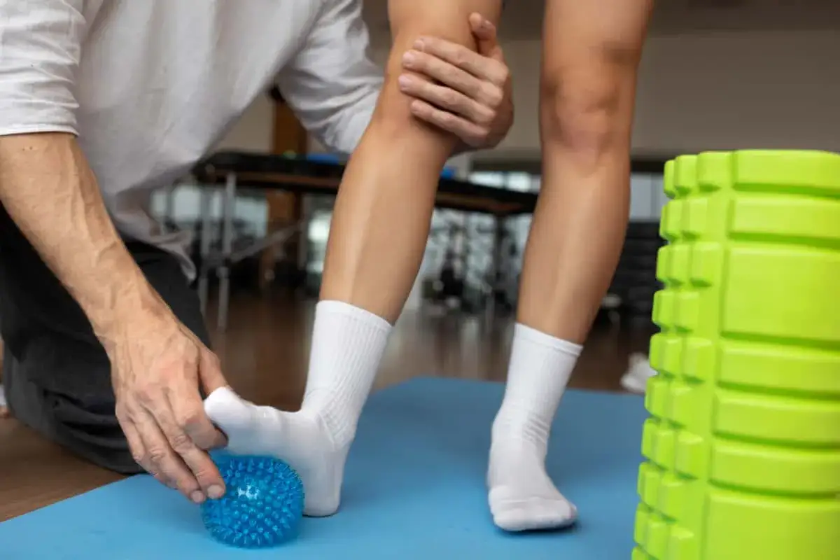 Fizjoterapeuta masuje stopę pacjenta niebieską piłeczką. Dowiadujemy się, skręcenie kostki 1 stopnia ile trwa.