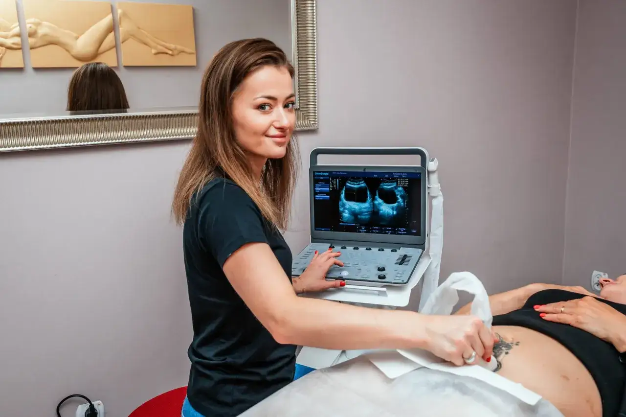 Fizjoterapeutka uroginekologiczna wykonuje badanie USG. Pacjentka leży na kozetce, a specjalistka przykłada głowicę aparatu do brzucha.