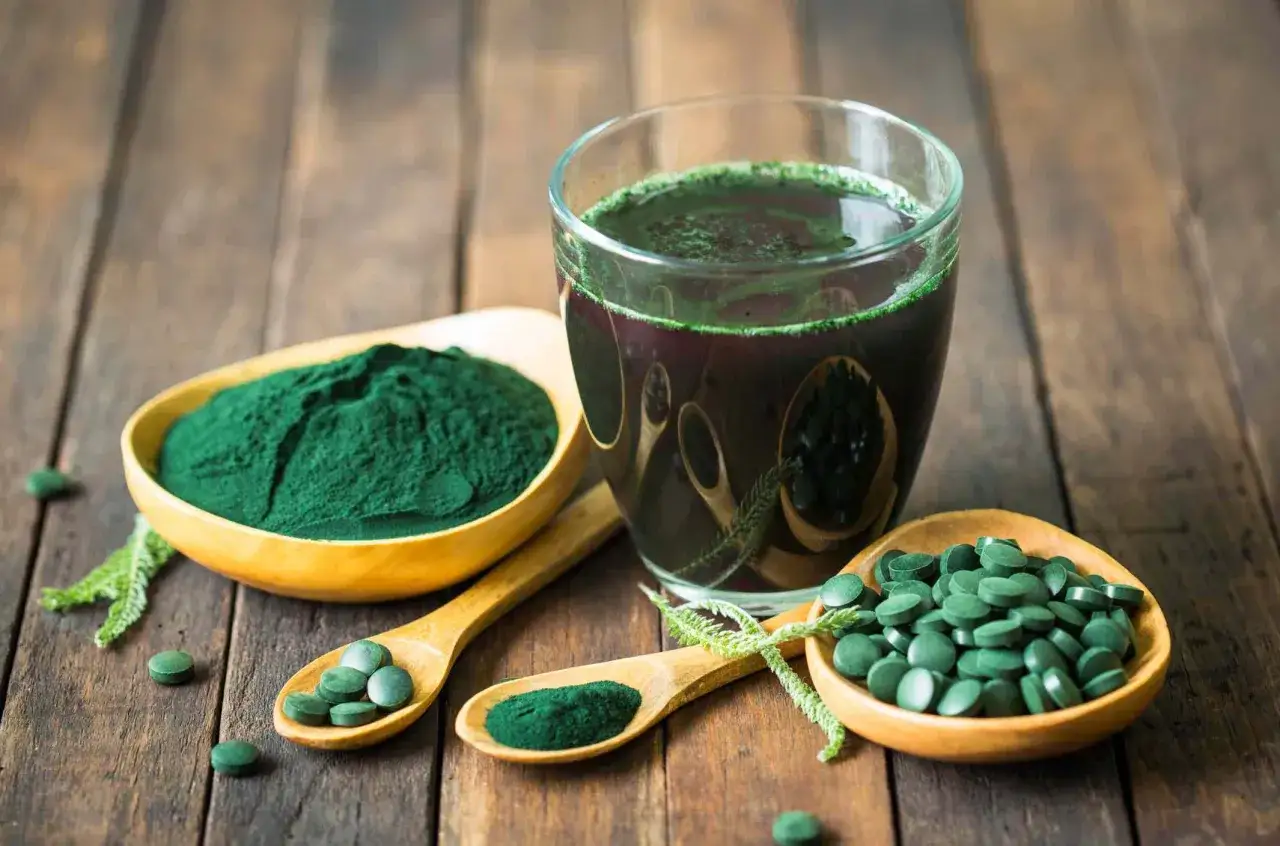 Zielony proszek i tabletki ze spiruliny i chlorelli, obok szklanki z napojem. Naturalne suplementy diety.