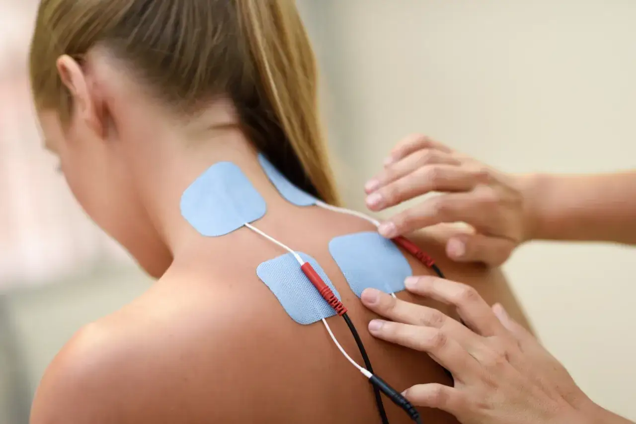 Fizjoterapeuta zakłada elektrody do elektrostymulacji na plecy pacjentki.