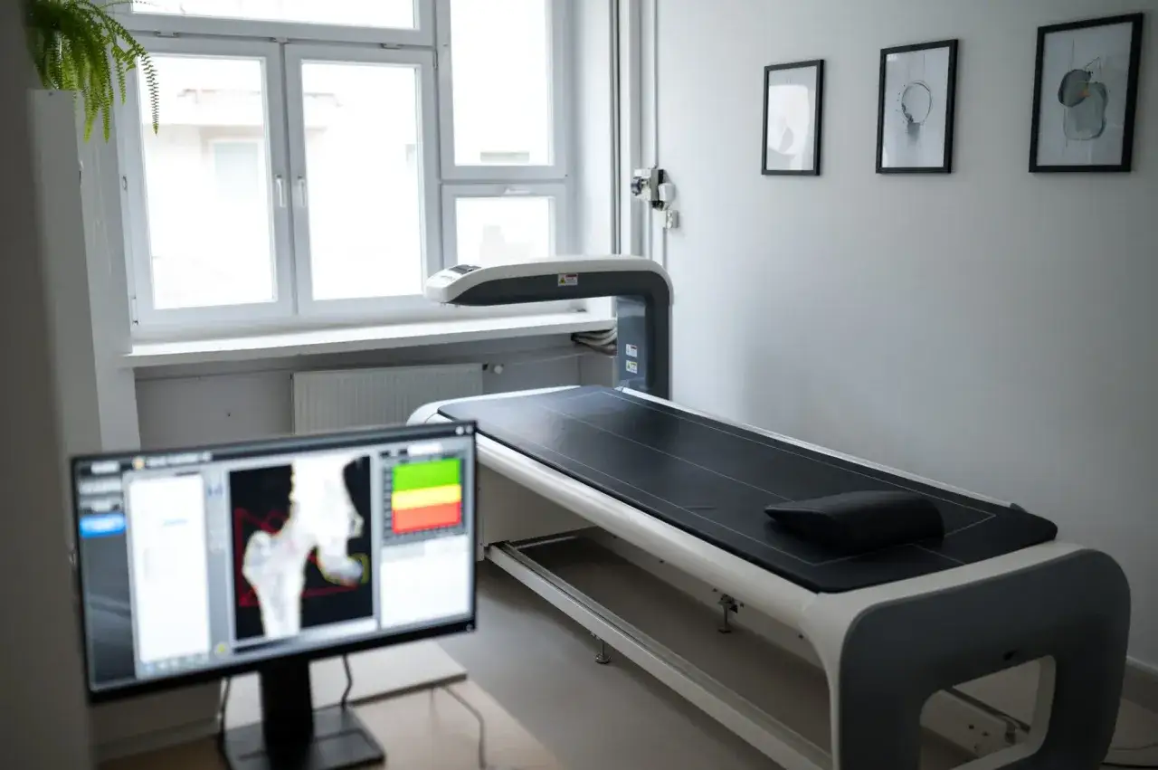 Gabinet z aparaturą do densytometrii. Na ekranie monitora wyniki badania kości, obok leżanka diagnostyczna.