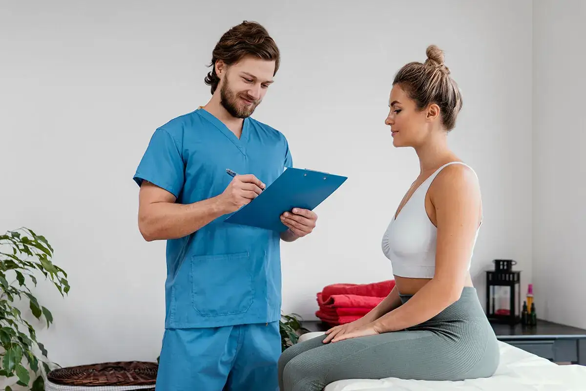 Fizjoterapeuta notuje na tablicy, rozmawiając z pacjentką. Czy u fizjoterapeuty trzeba się rozebrać? Zależy od zabiegu, ale często tak.