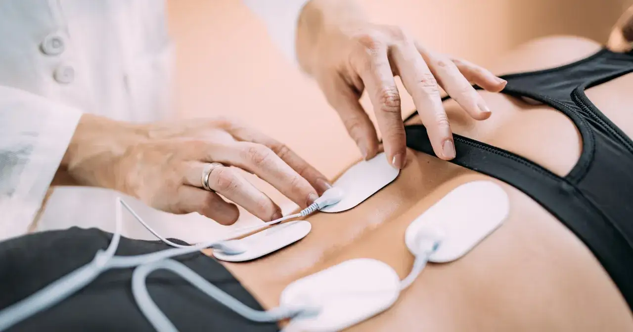 Rehabilitacja TENS: fizjoterapeuta umieszcza elektrody na plecach pacjenta, co jest częścią terapii prądami TENS.
