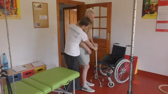 Terapeuta pomaga starszemu mężczyźnie wstać z pomocą balkonika. To kluczowy etap rehabilitacji po udarze, przywracający samodzielność.