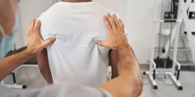 Fizjoterapeuta bada plecy pacjenta, szukając przyczyny bólu kręgosłupa piersiowego.