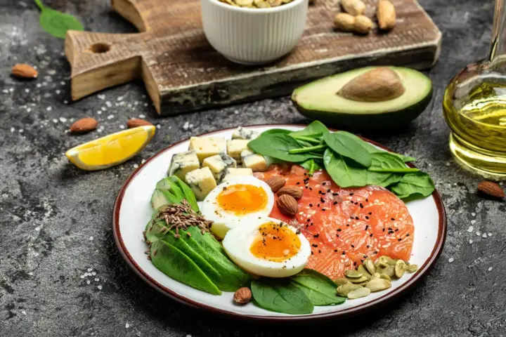 Talerz pełen zdrowych tłuszczów: łosoś, awokado, jajka, ser i orzechy. Idealne składniki na keto dietę.