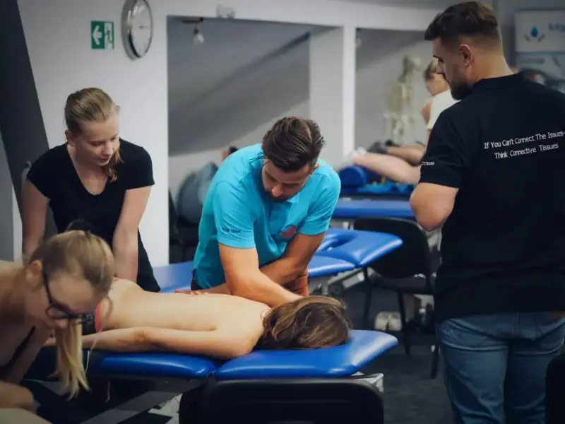 Uczestnicy szkolenia doskonalą technikę masażu tkanek głębokich, pracując nad plecami pacjenta.